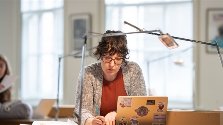 A person sat working in the reading room with a laptop and archive material.